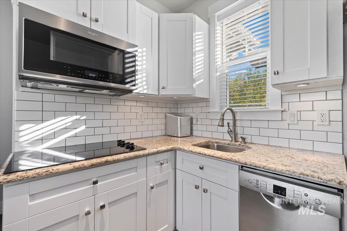 Kitchen with light stone counters, appliances with stainless steel finishes, white cabinetry, and decorative backsplash