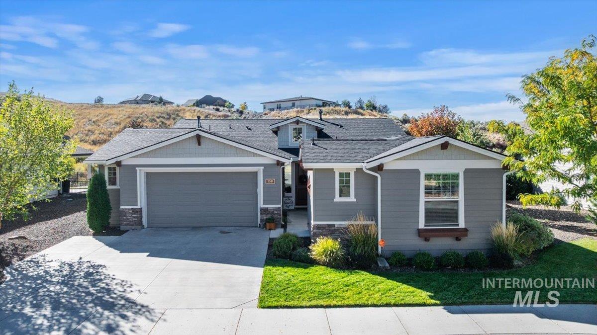 View of front of house featuring driveway, a shingled roof, a garage, stone siding, and a front yard