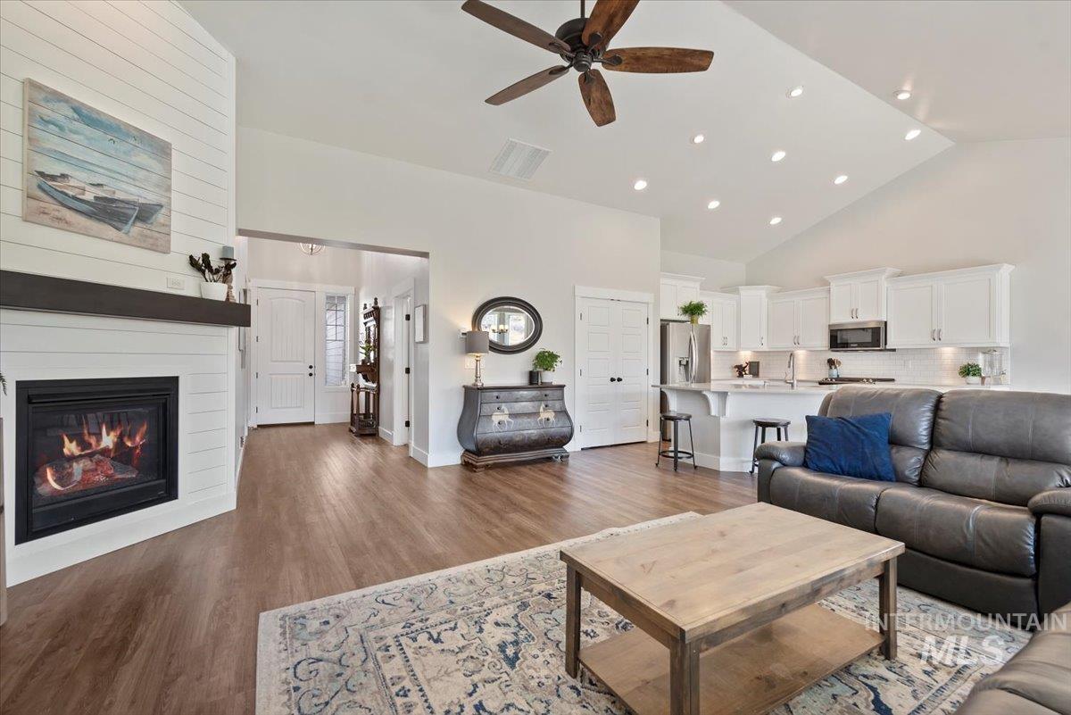 Living room featuring high vaulted ceiling, light wood-style flooring, recessed lighting, a ceiling fan, and a fireplace