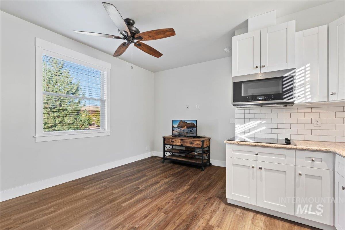Kitchen featuring white cabinetry, light stone counters, stainless steel microwave, dark wood finished floors, and tasteful backsplash