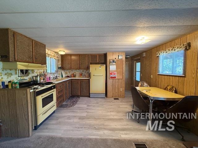 Kitchen featuring range with gas cooktop, freestanding refrigerator, light wood-style floors, wooden walls, and under cabinet range hood