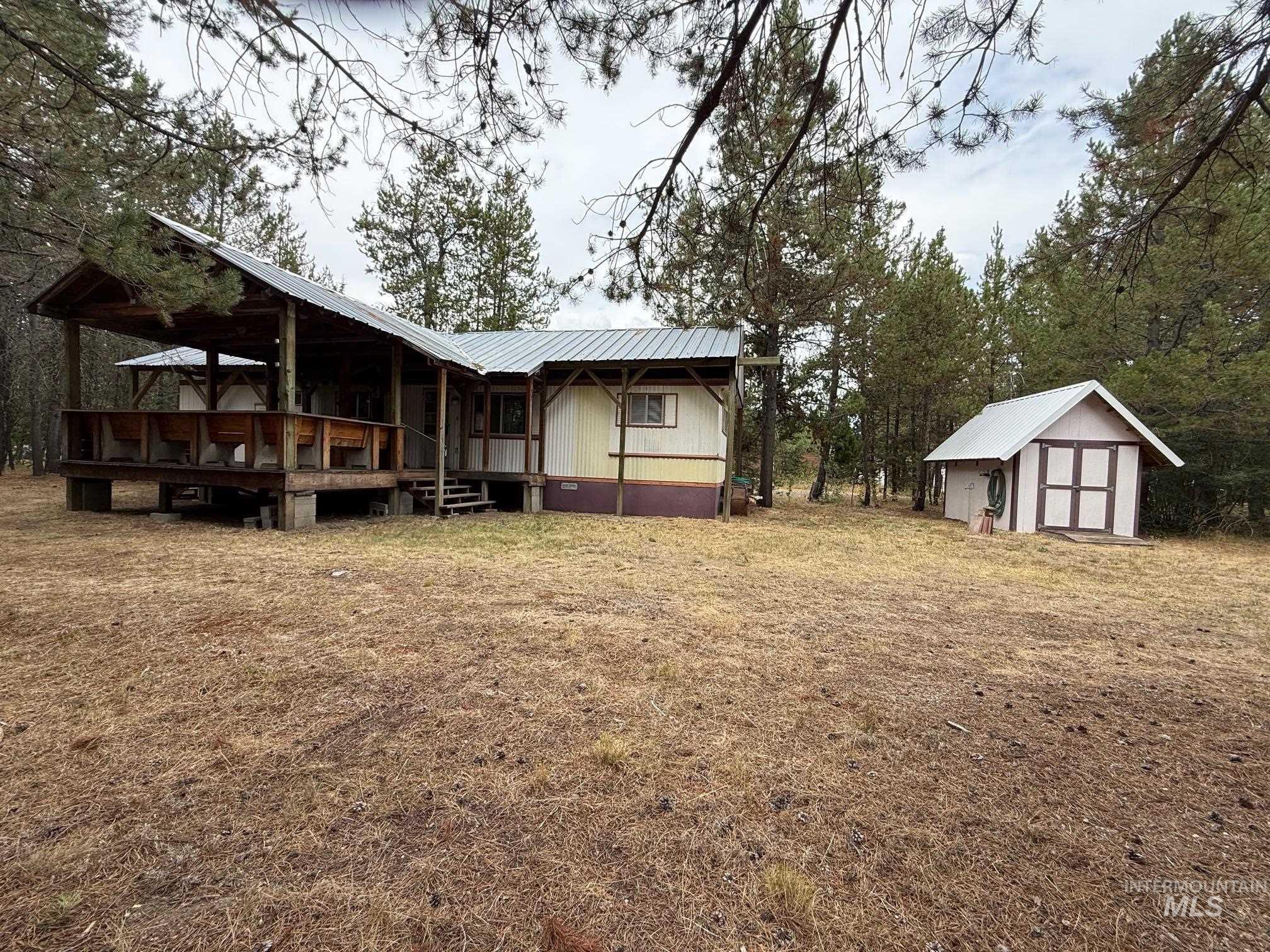 Back of house with a metal roof, a deck, a storage unit, and a yard
