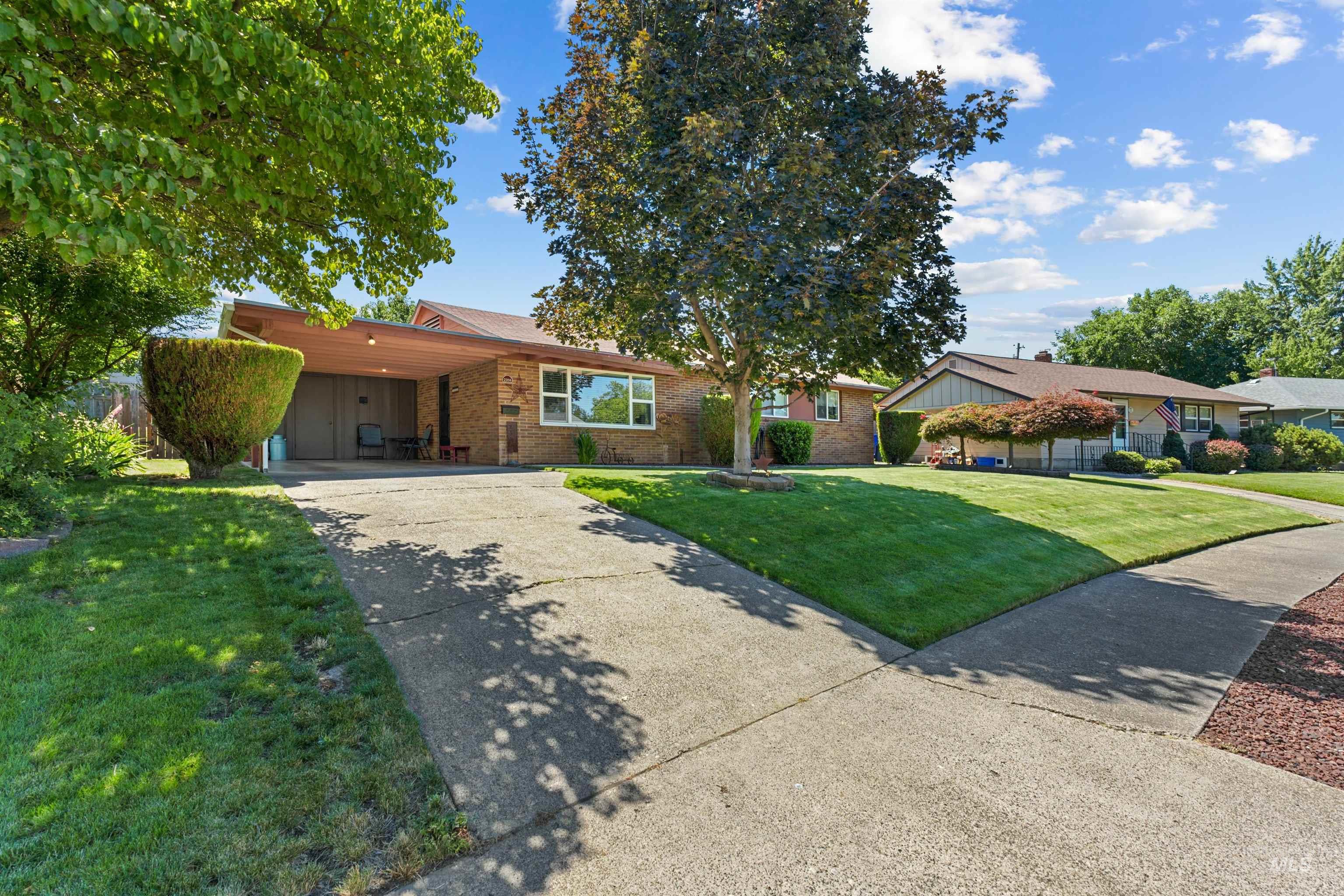 Brick facade single-story residence featuring a covered carport and an extended driveway