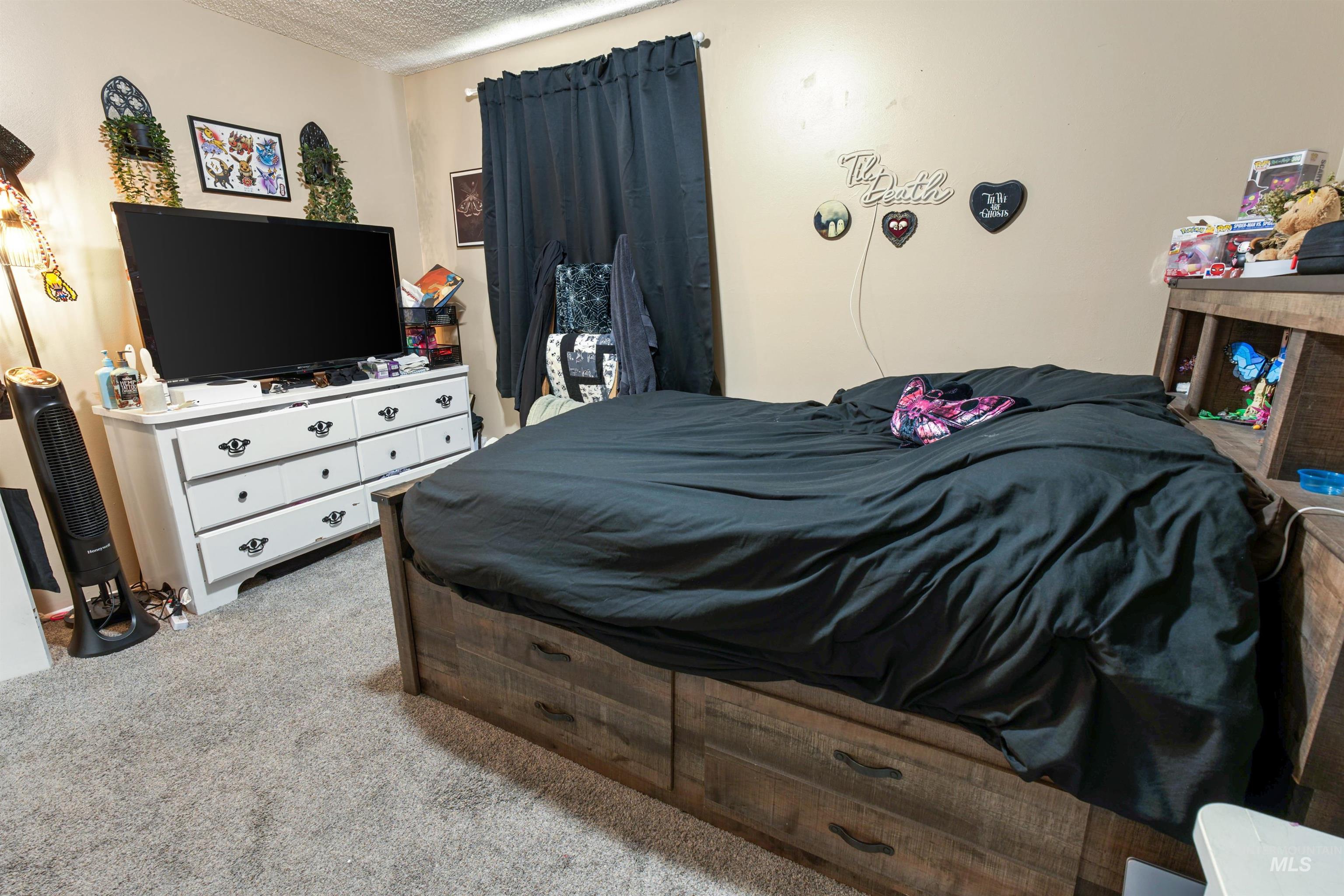 Carpeted interior space featuring a wood-finish bed frame with integrated storage drawers, a coordinating wood-finish headboard with built-in shelving, and light-toned walls