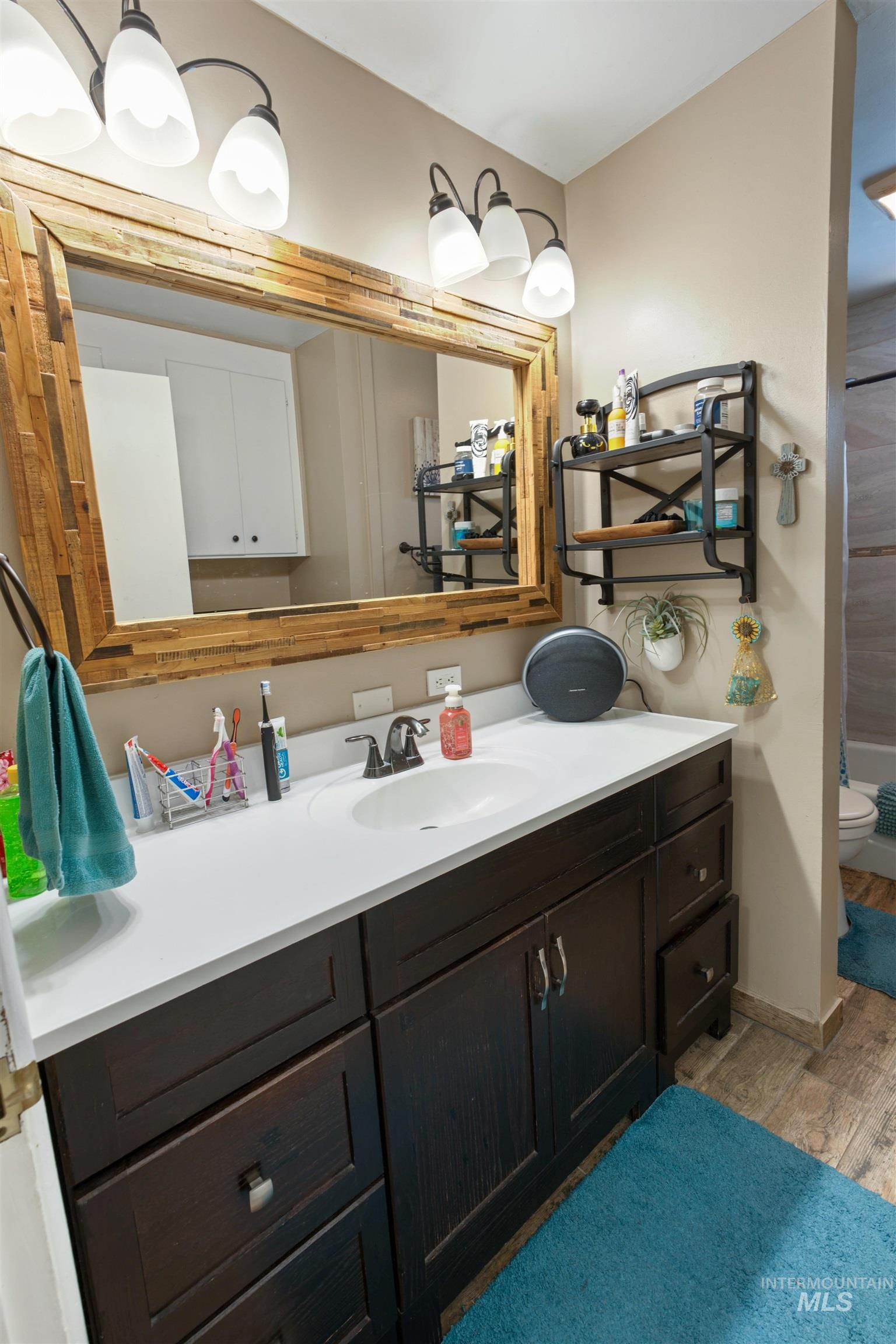 Vanity featuring a wood-framed mirror with overhead lighting, a white countertop, an undermount sink with a dark-finish faucet, and dark wood-finish cabinetry