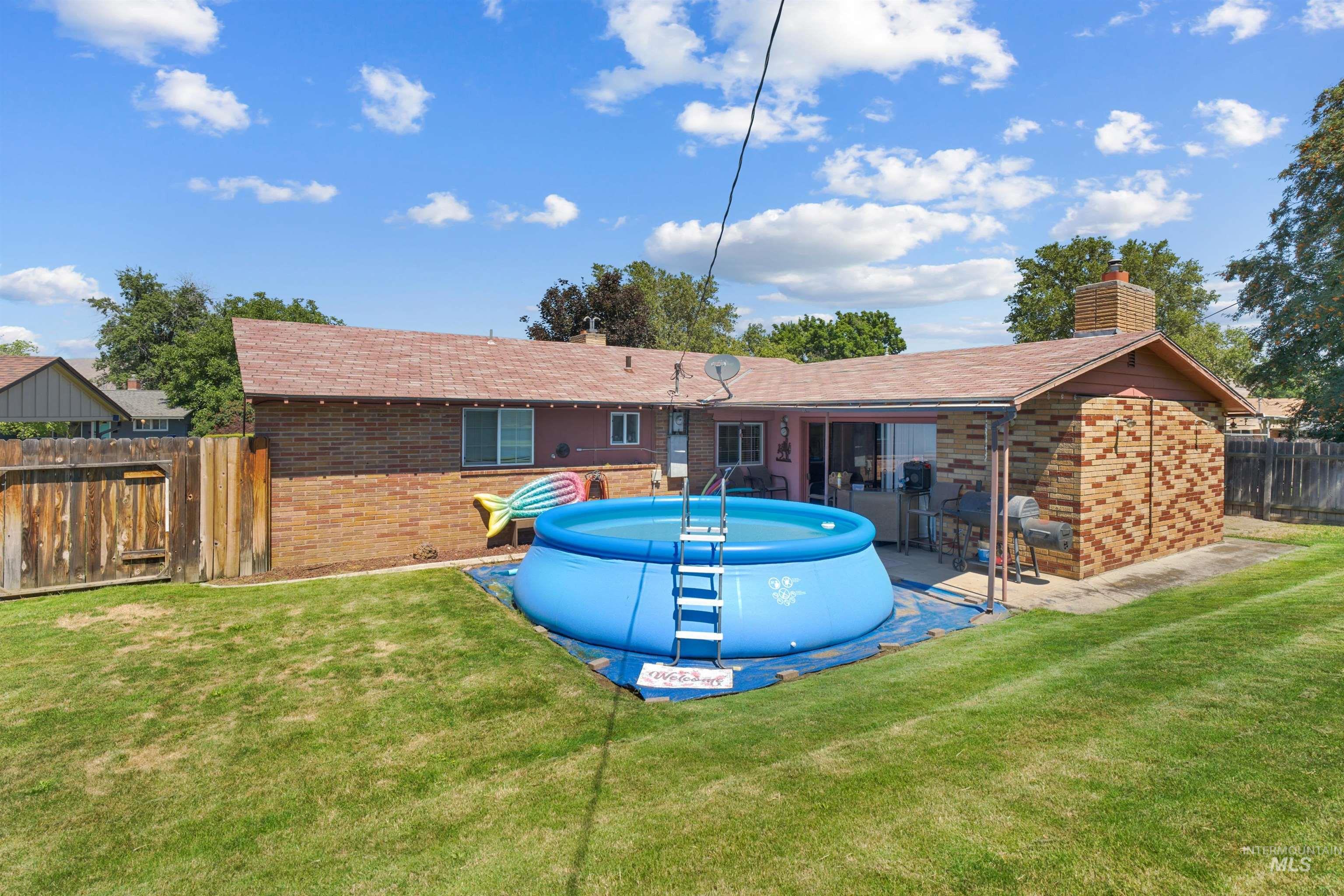 Expansive backyard featuring a manicured lawn, brick exterior, wood fence, and a covered patio area