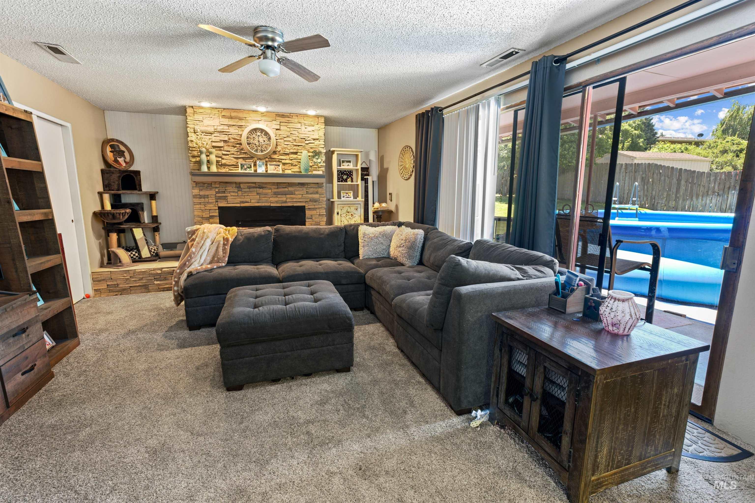Living space featuring a stacked stone fireplace with a substantial hearth, ceiling fan, and direct access to an outdoor patio with a visible pool