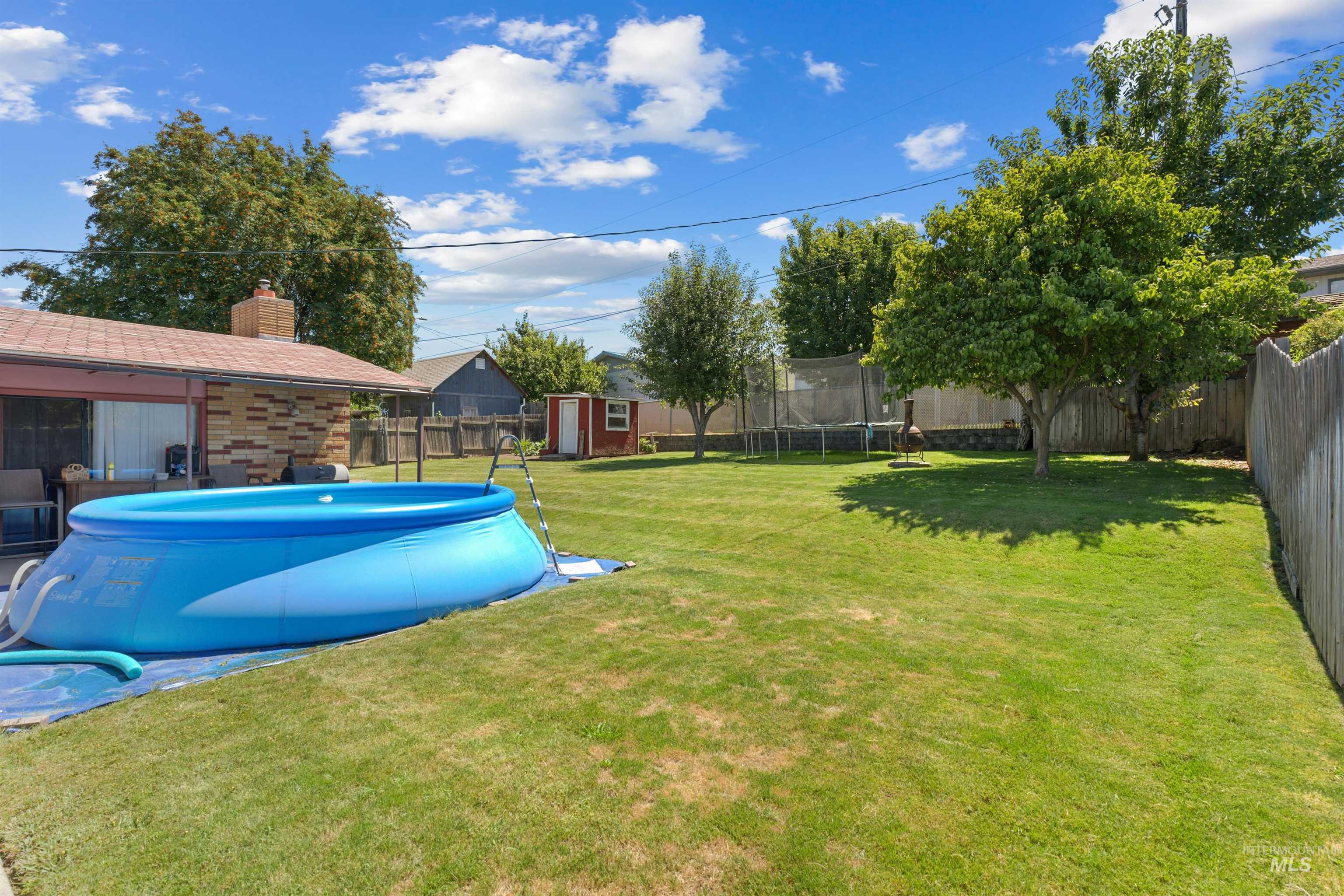 Spacious backyard featuring a manicured lawn, established trees, and a wooden privacy fence
