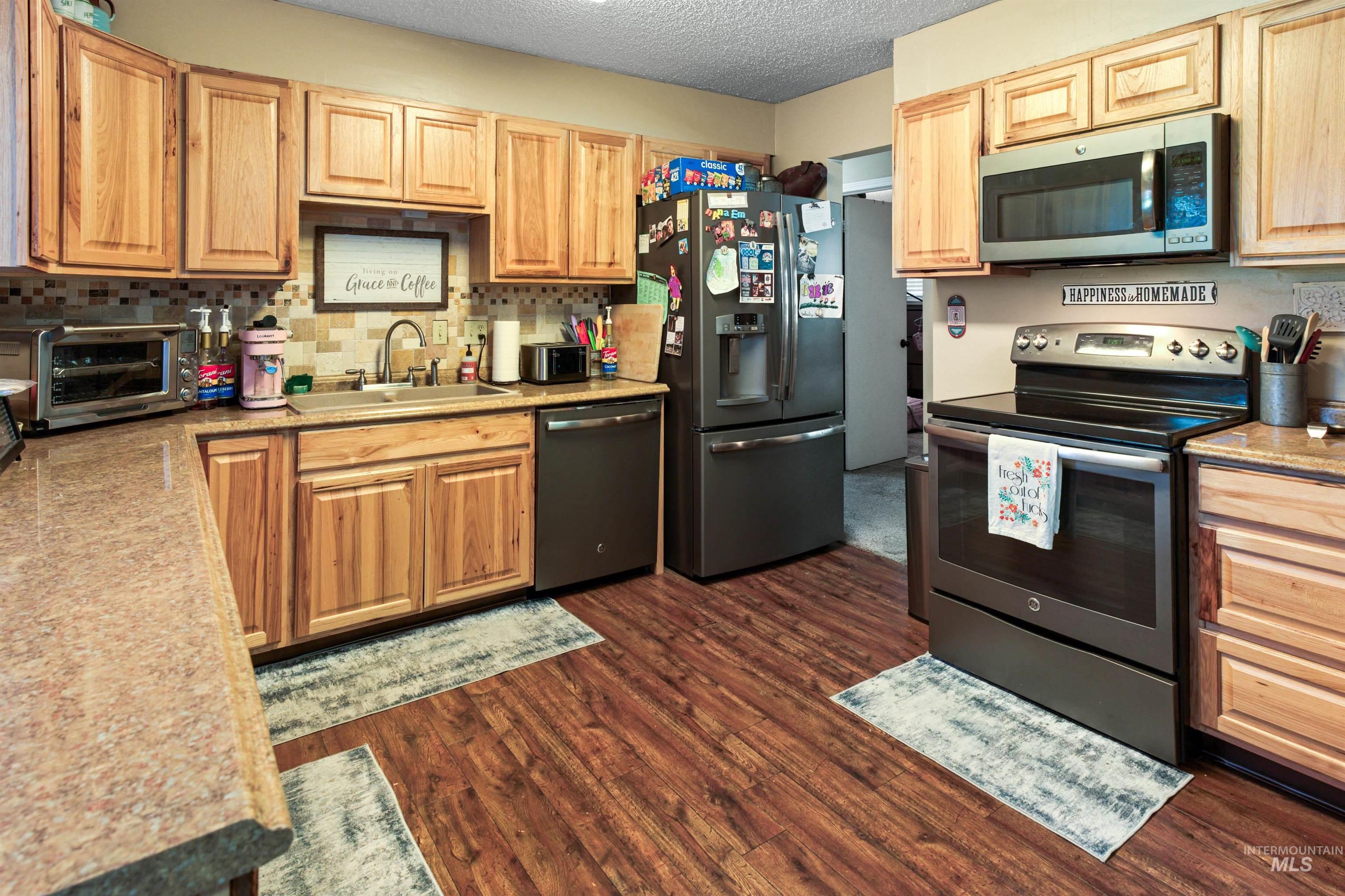 Kitchen featuring wood-finish flooring, light wood cabinetry, stone-look countertops, and a tiled backsplash