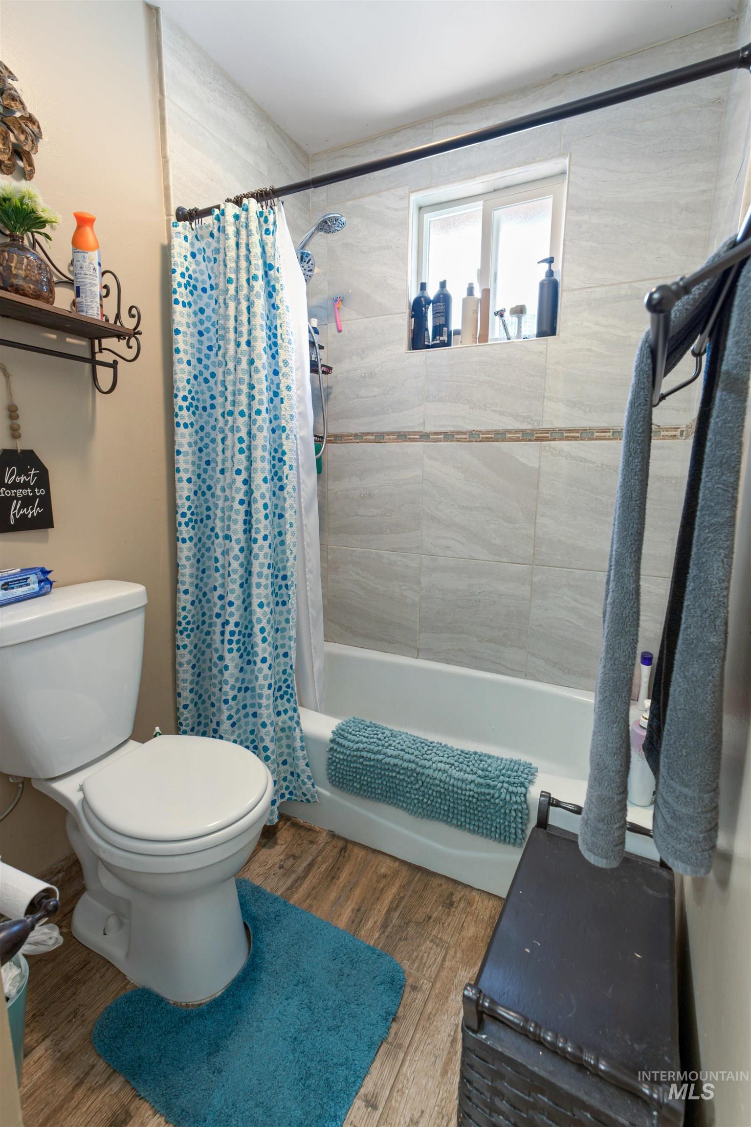 Bathroom with a white tub and shower combination featuring light-toned large format wall tiling and a decorative accent tile band