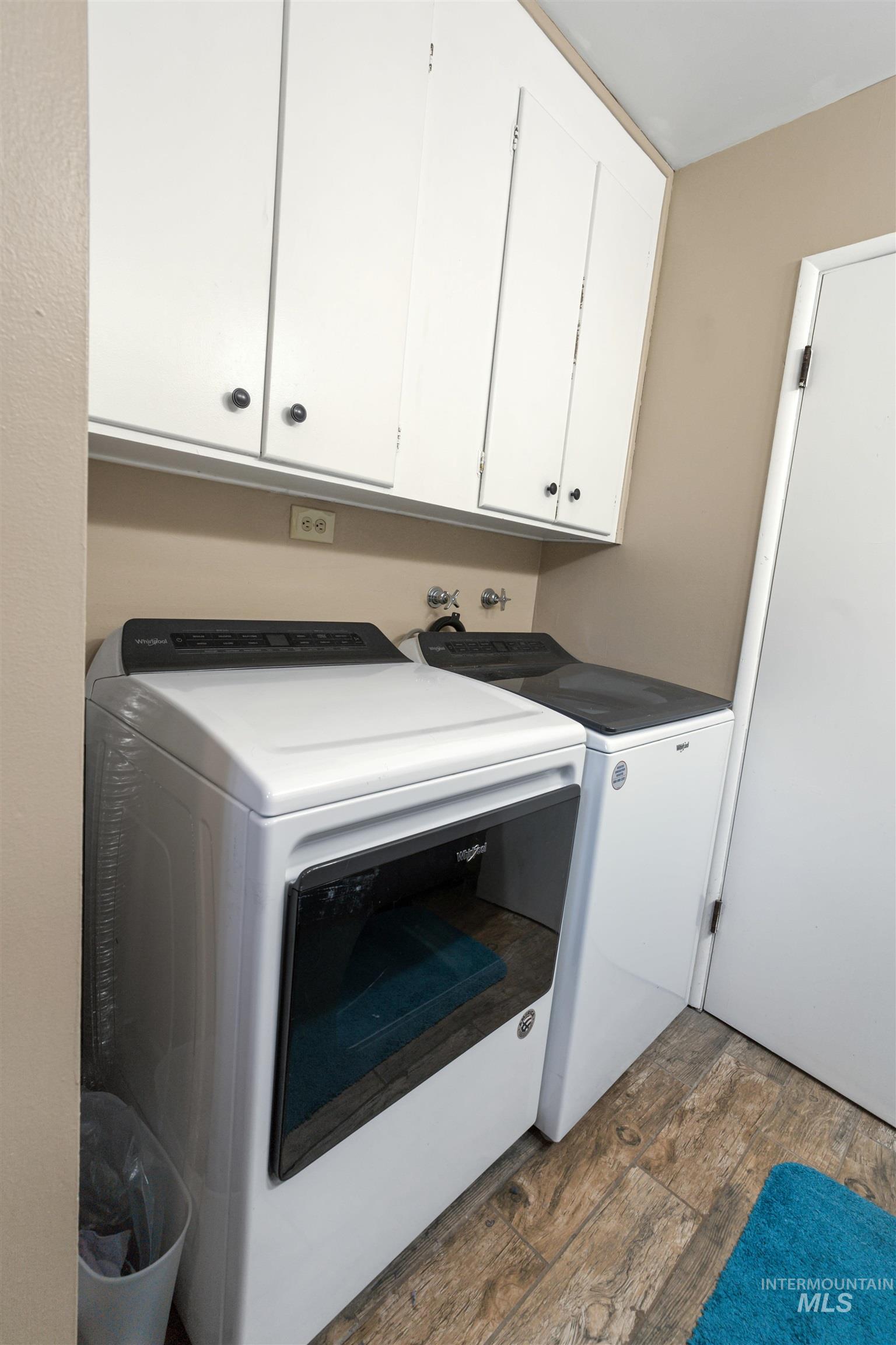 Laundry area featuring wood-finish flooring, overhead white cabinetry, and neutral wall paint