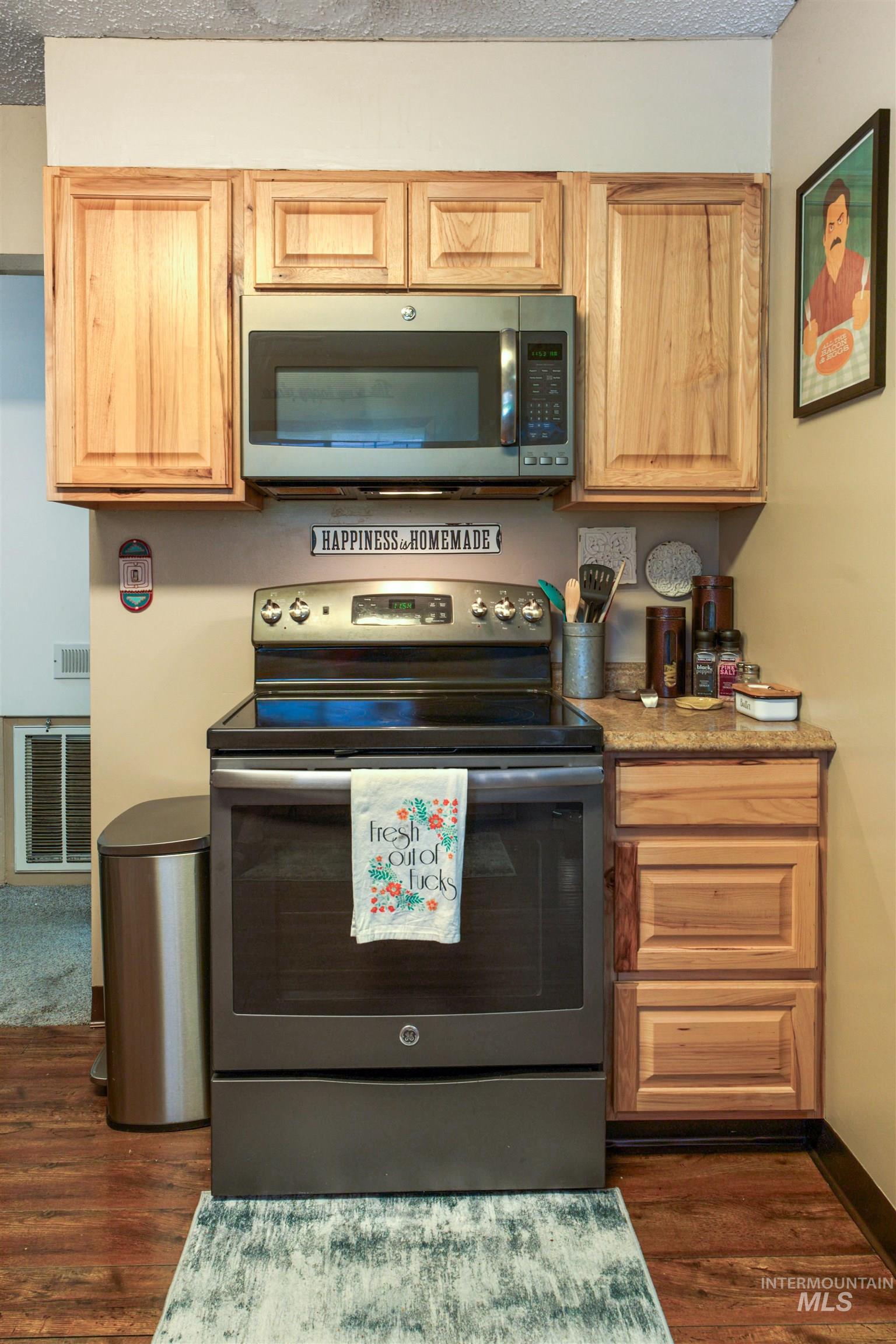 Kitchen features a stainless steel range with a built-in microwave above, light wood cabinetry, stone-finish countertops, and wood-finish flooring