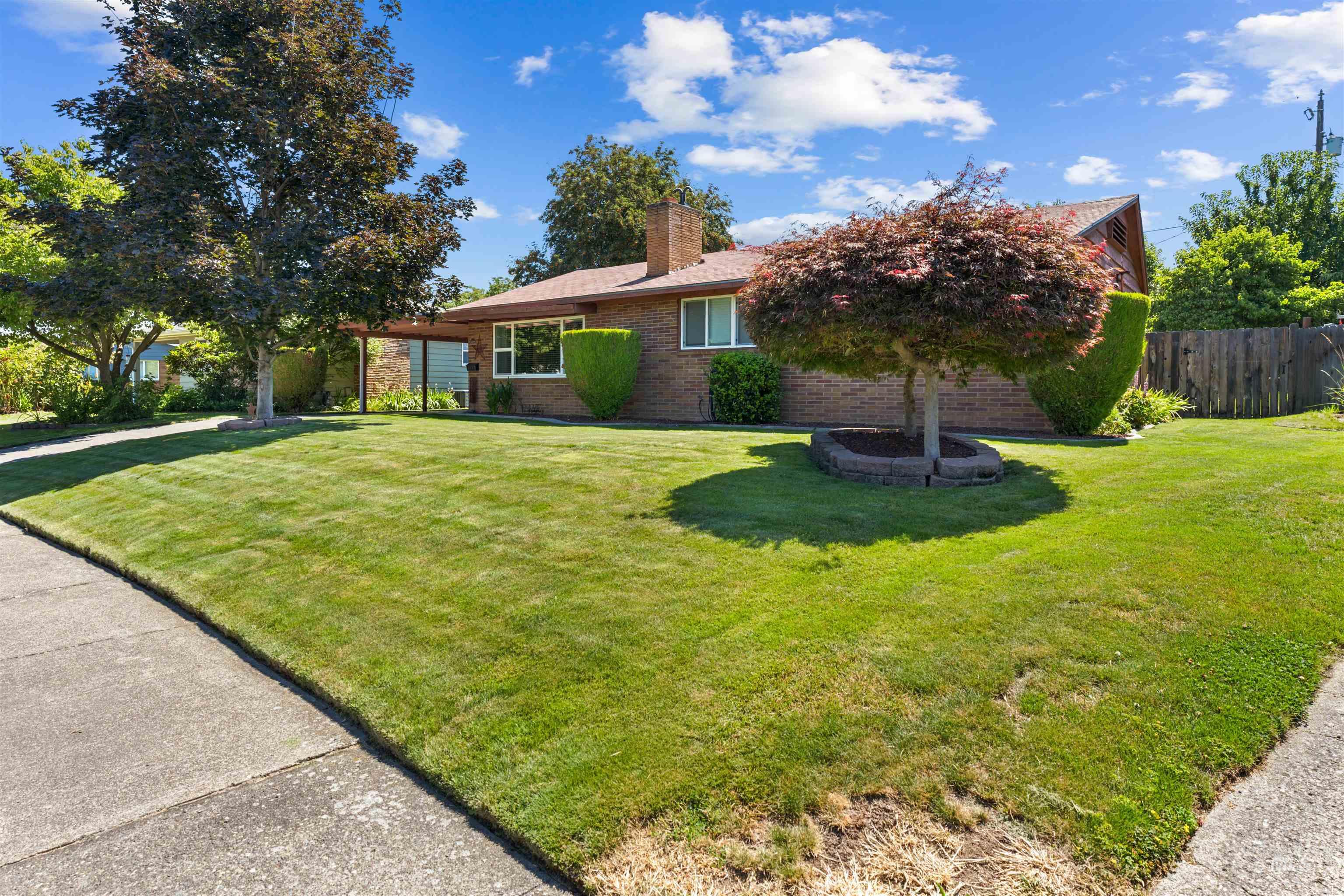 Expansive front lawn with mature trees and a decorative, brick-lined tree bed