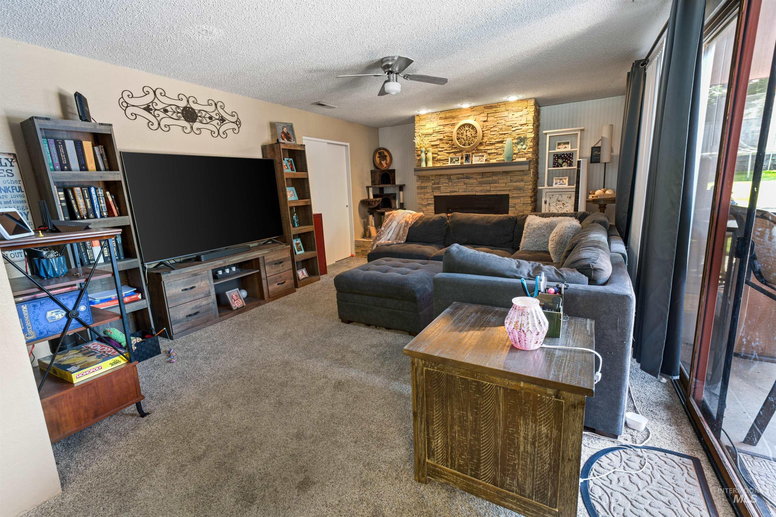 Living room featuring a stacked stone fireplace with a stone hearth and wood mantel