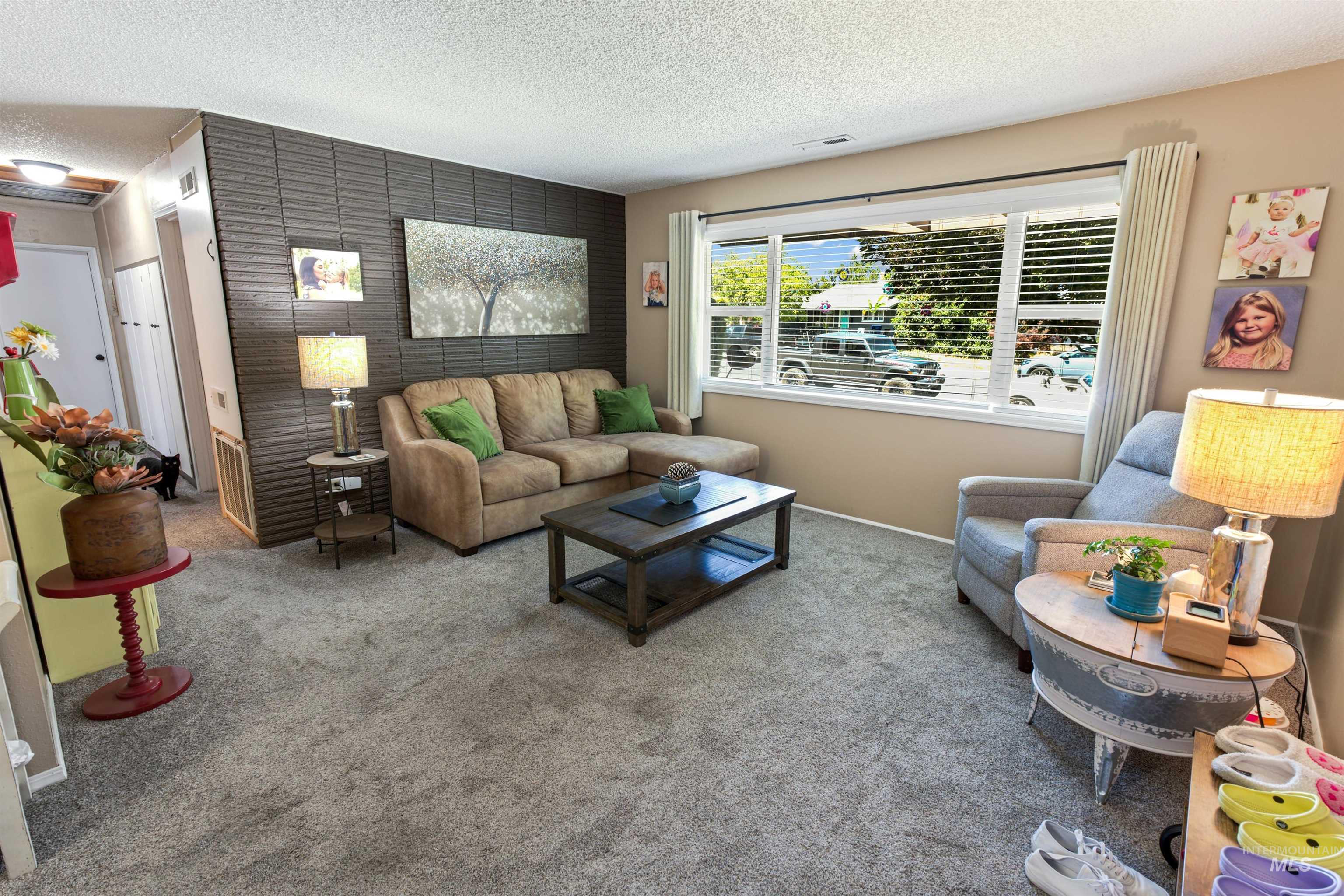 Living area featuring a textured accent wall, light beige wall paint, and gray carpet flooring