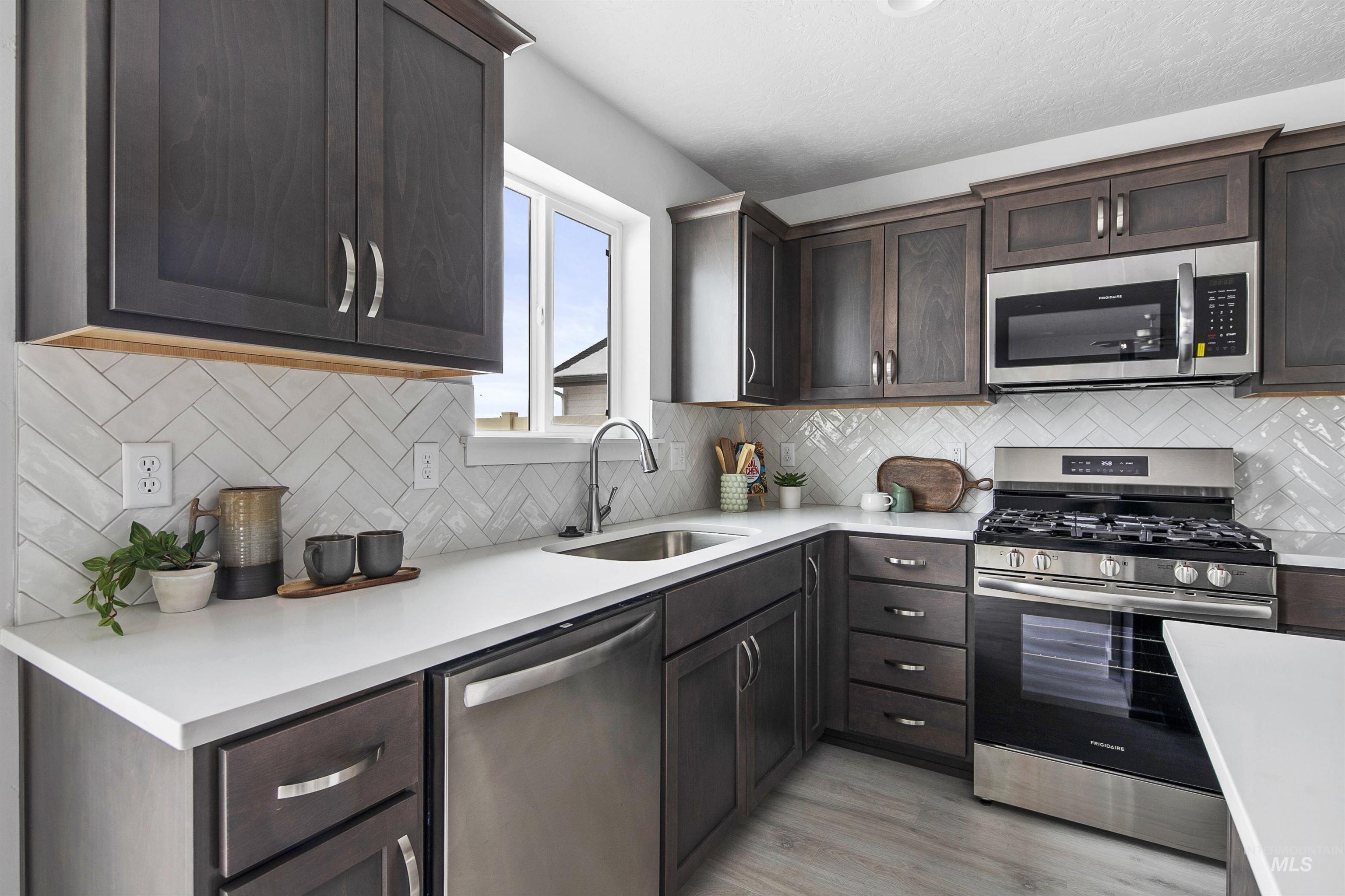 Kitchen featuring stainless steel appliances, dark brown cabinets, light wood-style flooring, light stone counters, and backsplash