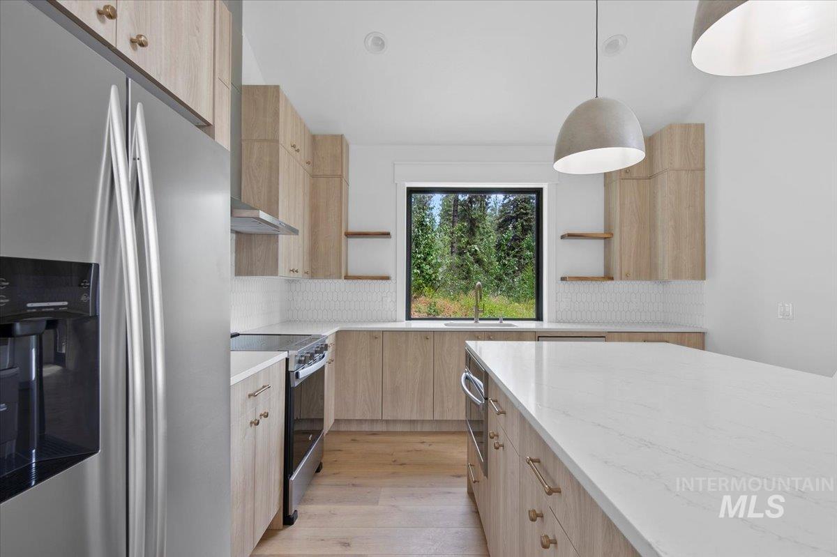 Kitchen with light brown cabinets, open shelves, appliances with stainless steel finishes, modern cabinets, and light wood-style flooring