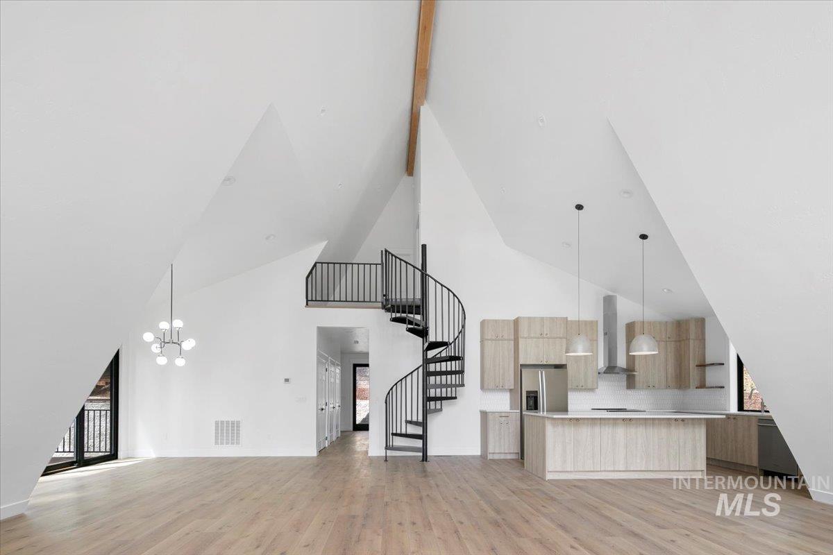 Unfurnished living room with high vaulted ceiling, light wood-style floors, stairway, and a chandelier
