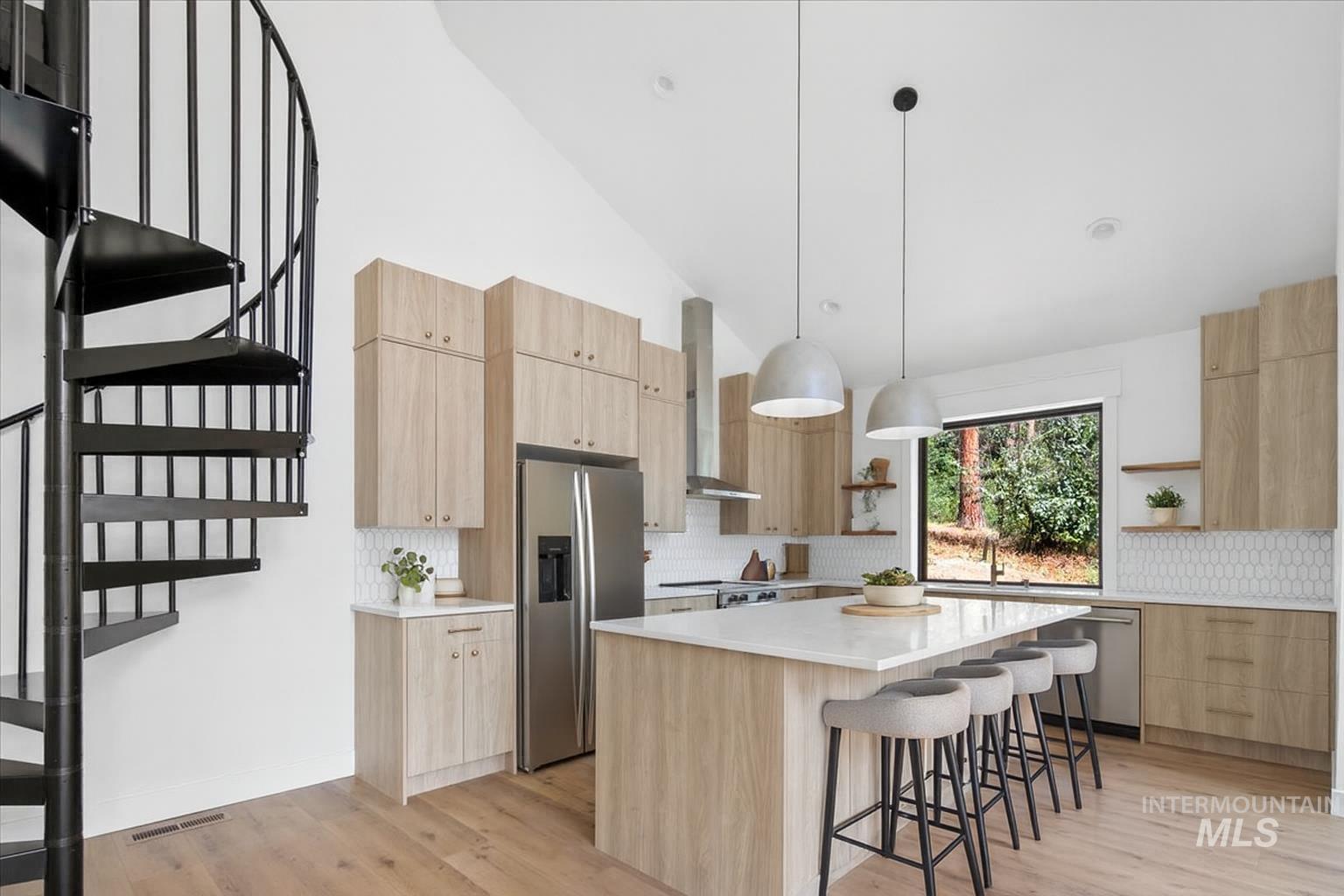 Kitchen with light brown cabinets, open shelves, a kitchen bar, decorative light fixtures, and high vaulted ceiling