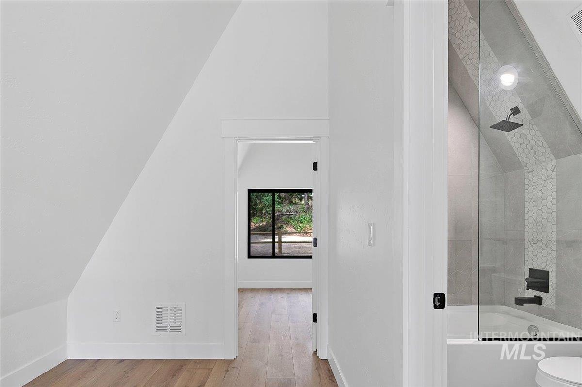 Bathroom with bath / shower combo with glass door, vaulted ceiling, and wood finished floors