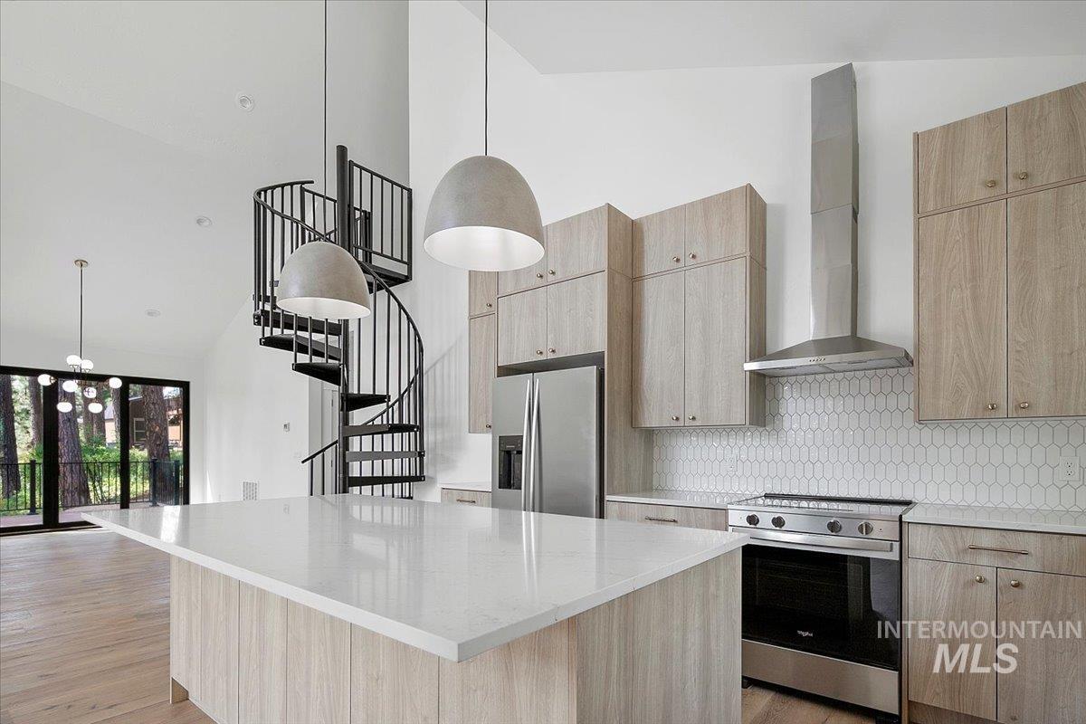 Kitchen with appliances with stainless steel finishes, wall chimney exhaust hood, high vaulted ceiling, a kitchen island, and decorative backsplash