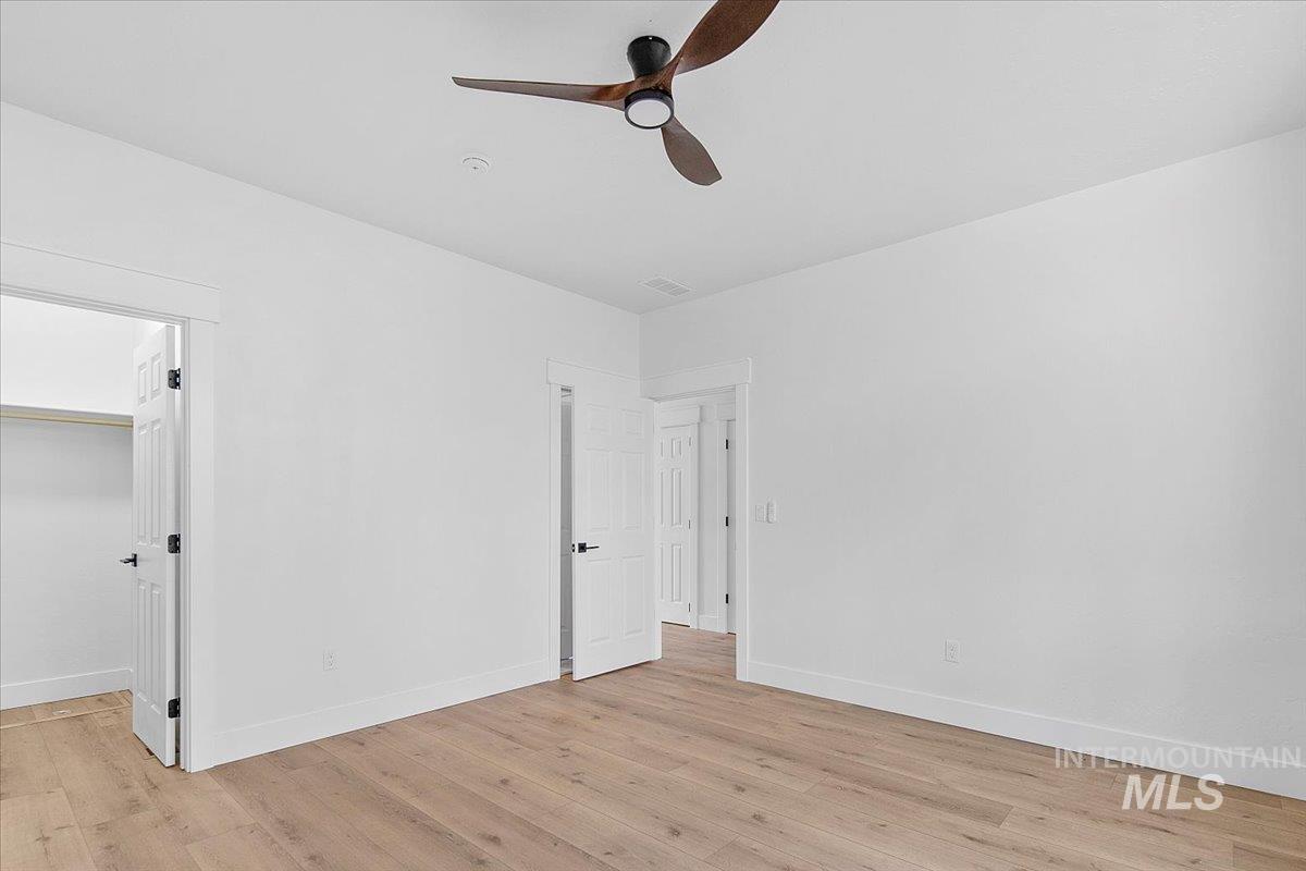 Unfurnished bedroom with light wood-type flooring, a spacious closet, and ceiling fan