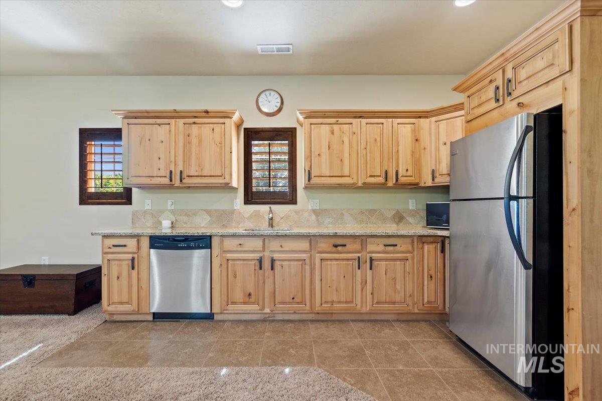 Kitchen featuring appliances with stainless steel finishes, light brown cabinetry, healthy amount of natural light, and light stone counters