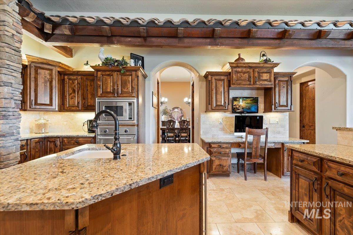 Kitchen with appliances with stainless steel finishes, arched walkways, tasteful backsplash, and light stone countertops