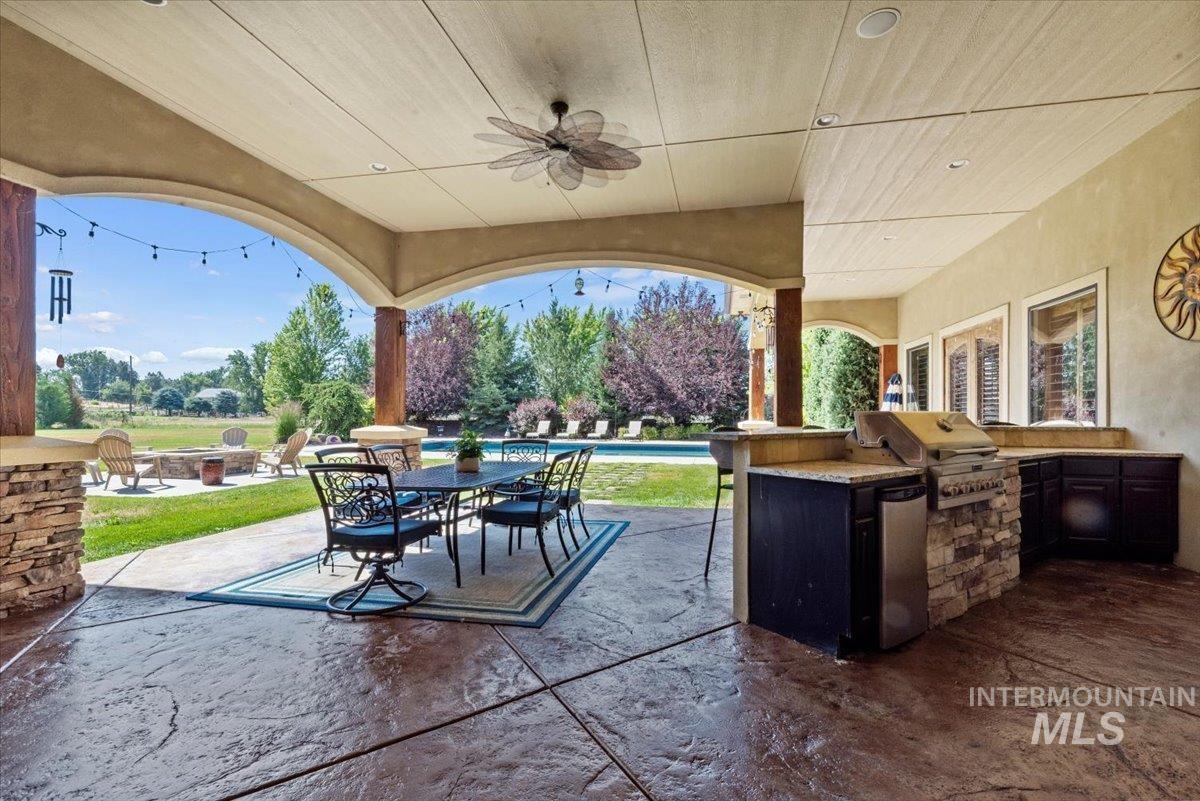 View of patio / terrace with a fire pit, an outdoor kitchen, an outdoor pool, a ceiling fan, and outdoor dining space