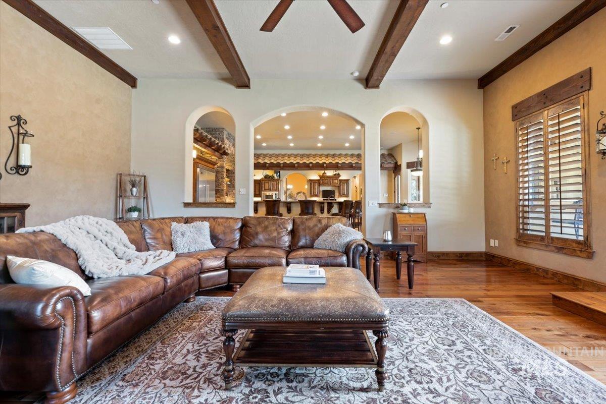 Living area featuring wood finished floors, arched walkways, beam ceiling, ceiling fan, and recessed lighting