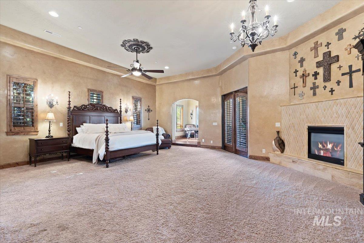 Carpeted bedroom with arched walkways, a chandelier, a premium fireplace, and recessed lighting