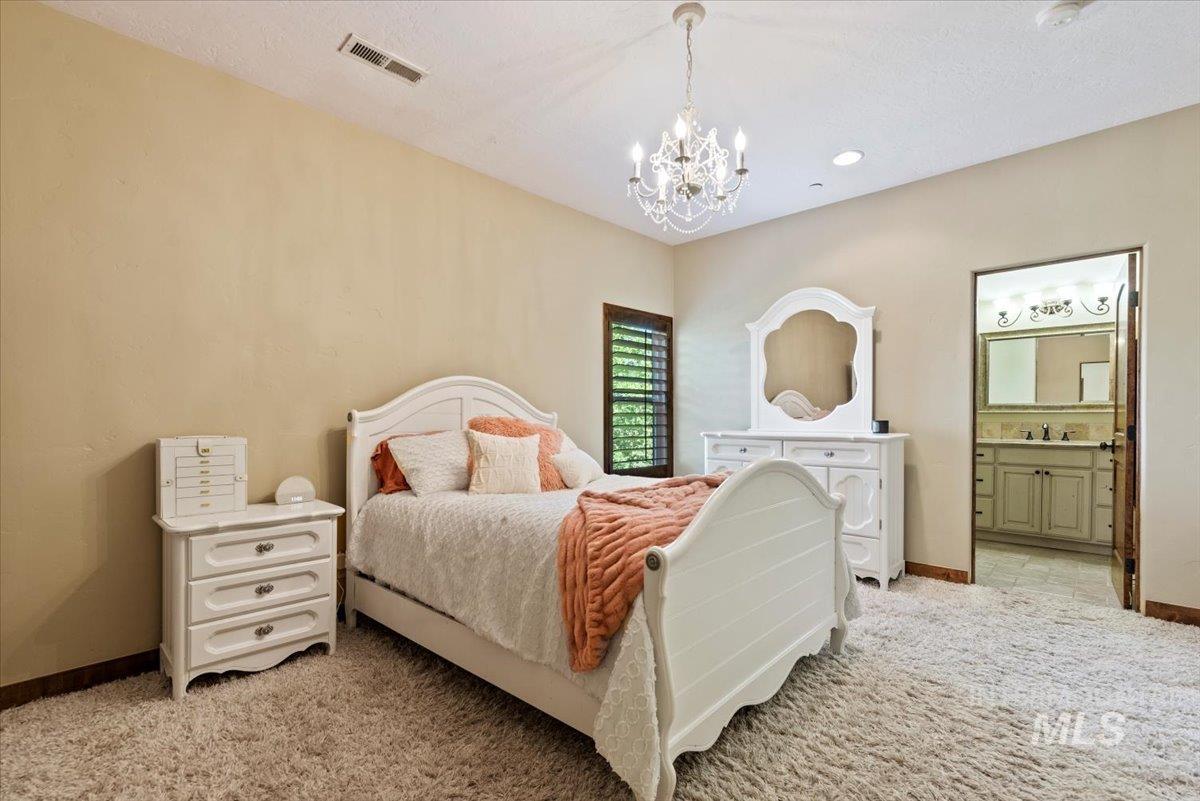 Bedroom featuring a chandelier, light carpet, and connected bathroom