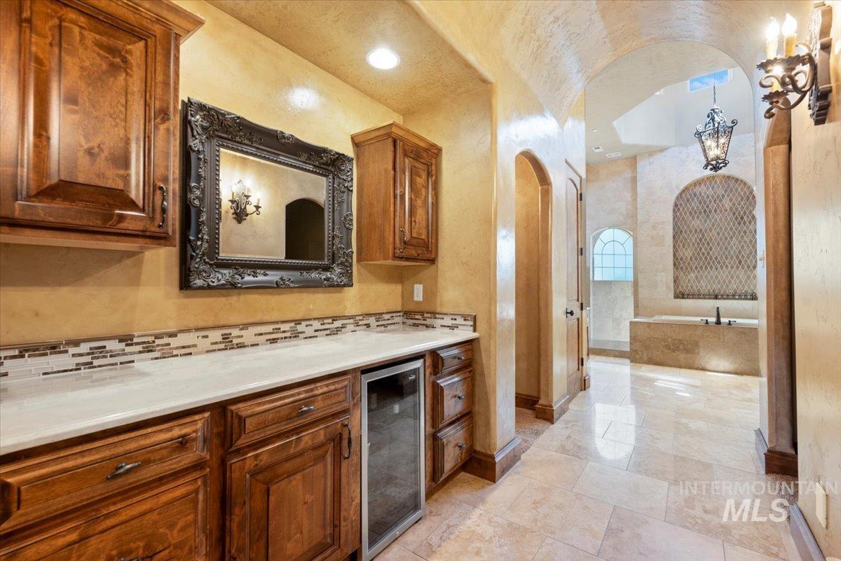 Kitchen featuring wine cooler, arched walkways, backsplash, light countertops, and brown cabinetry