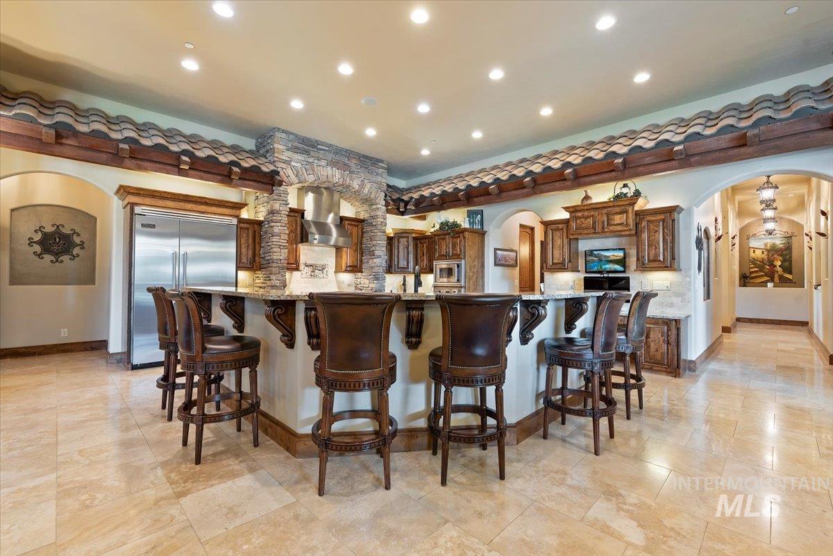 Kitchen featuring arched walkways, built in appliances, island exhaust hood, decorative backsplash, and recessed lighting