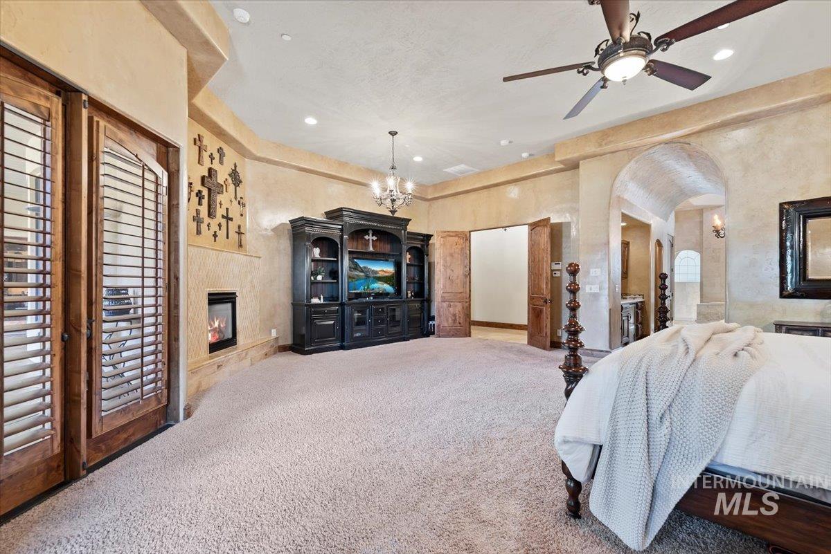Carpeted bedroom featuring a glass covered fireplace, arched walkways, recessed lighting, and a chandelier