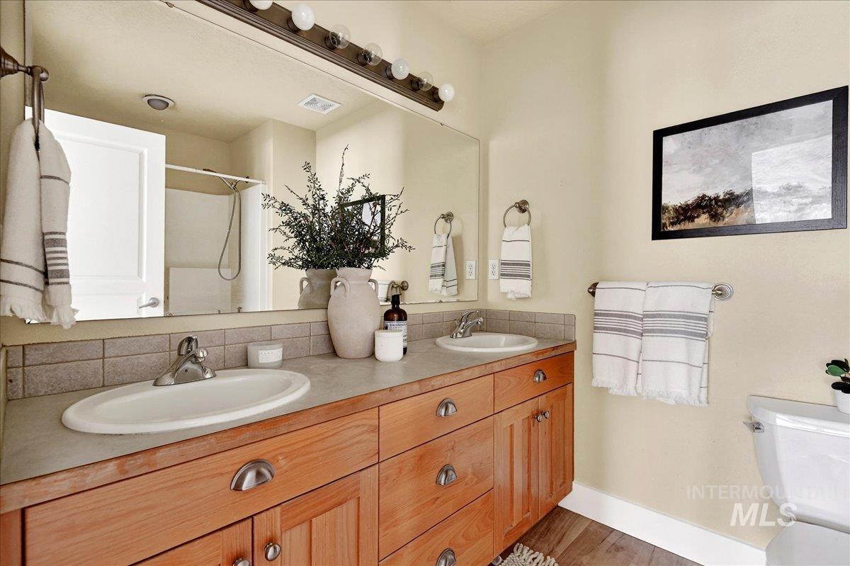 Bathroom featuring a shower with curtain, double vanity, light wood-type flooring, and tasteful backsplash