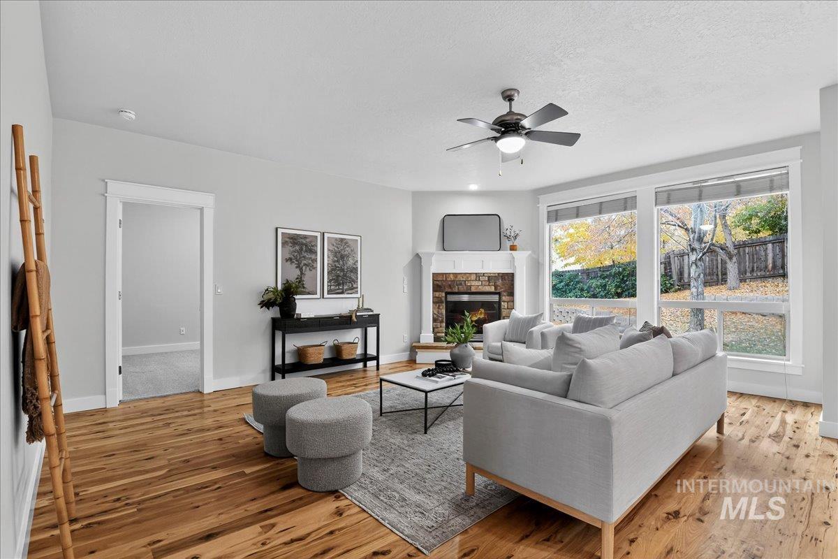 Living room featuring a fireplace, light wood finished floors, a ceiling fan, and a textured ceiling