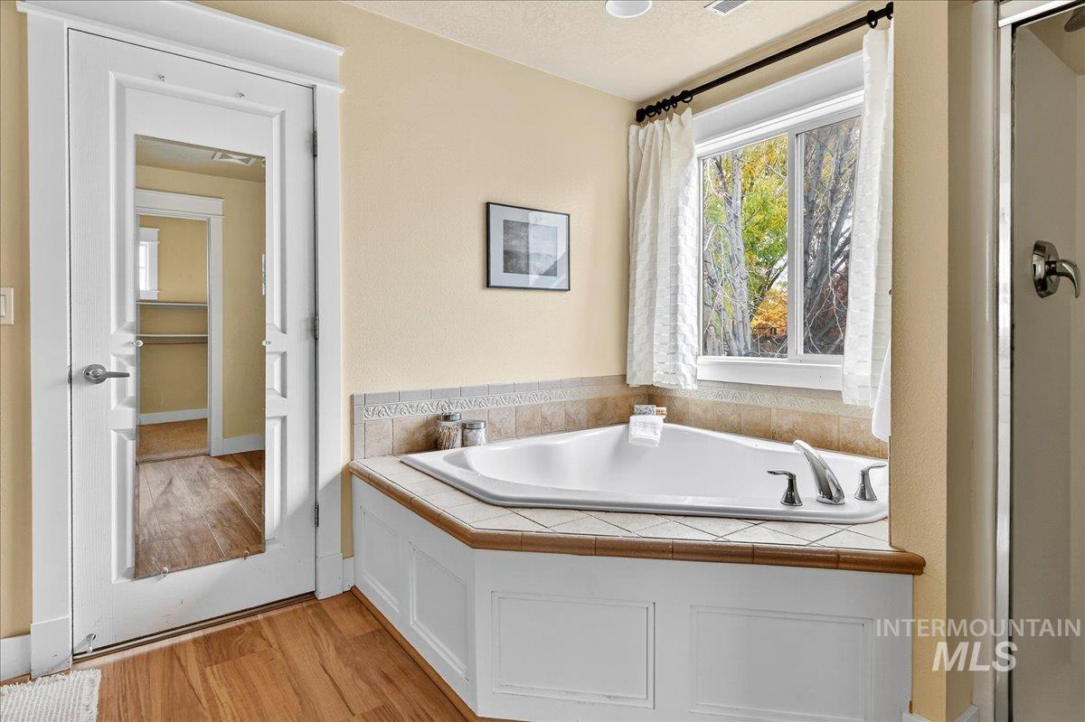 Full bath with light wood finished floors, a garden tub, and a stall shower