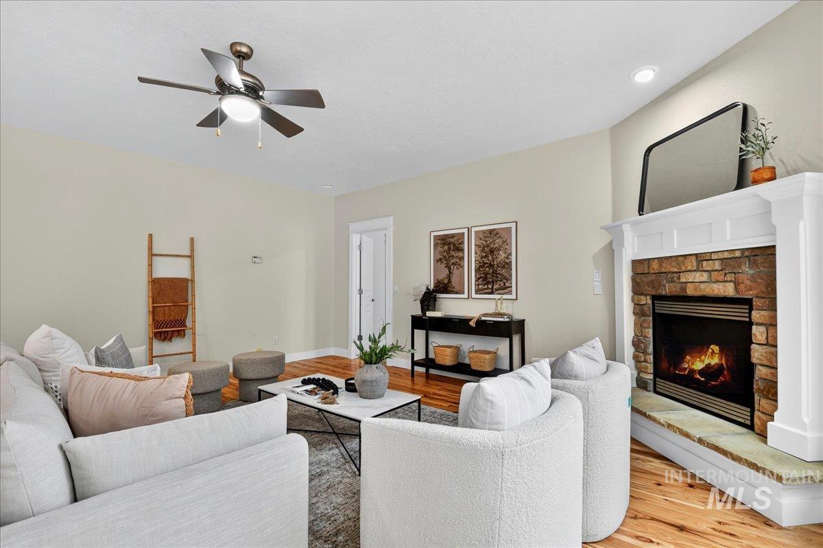 Living room featuring wood finished floors, a warm lit fireplace, and a ceiling fan