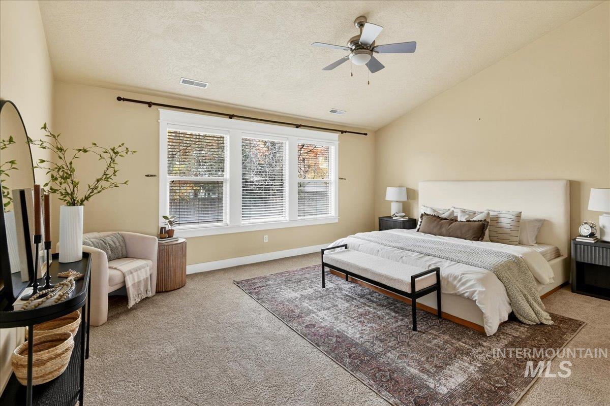 Carpeted bedroom with a textured ceiling, vaulted ceiling, and a ceiling fan
