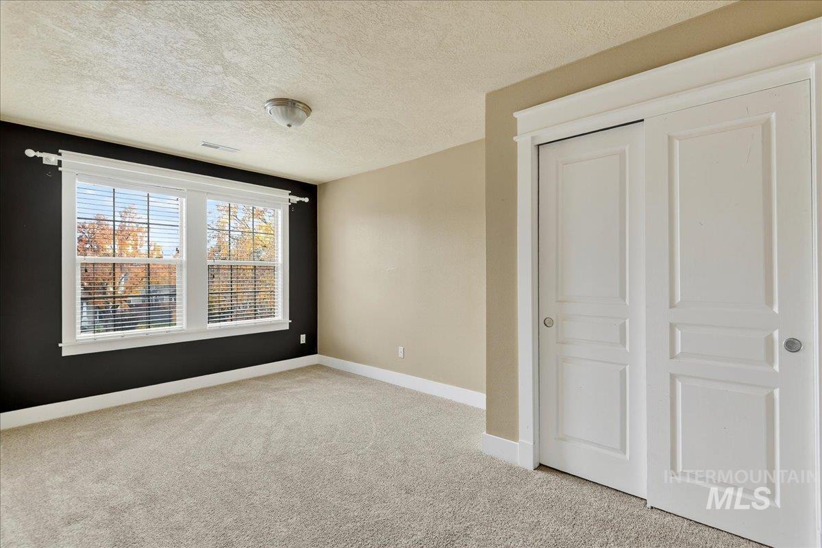 Unfurnished bedroom with a textured ceiling, light carpet, and a closet