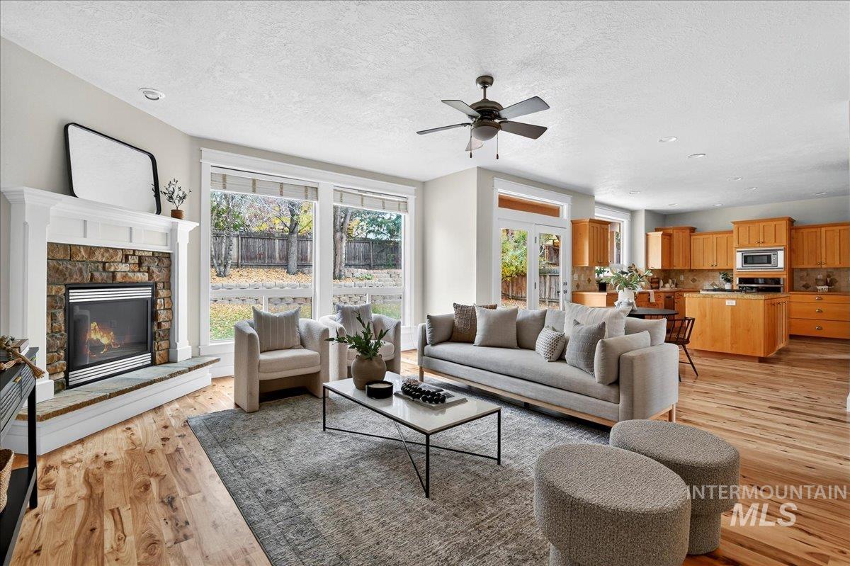 Living room featuring a fireplace, light wood-type flooring, a textured ceiling, healthy amount of natural light, and ceiling fan