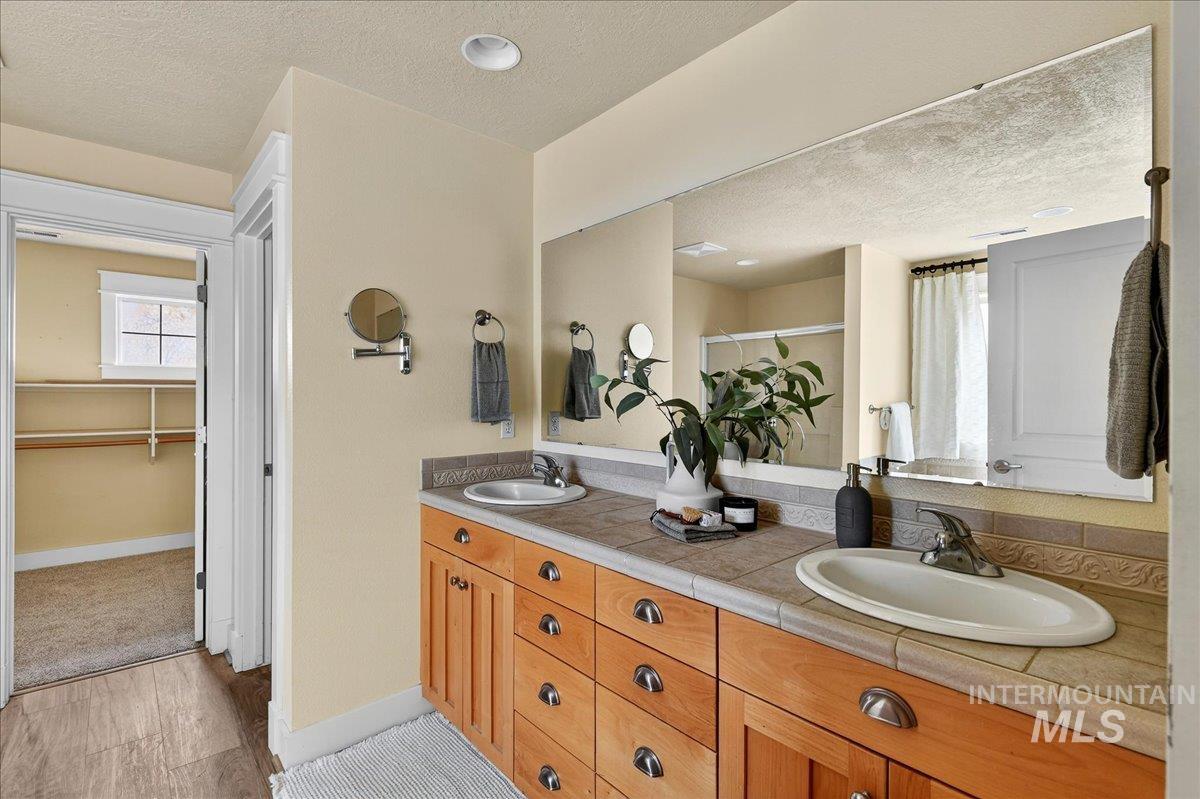 Full bathroom with curtained shower, double vanity, a spacious closet, and a textured ceiling