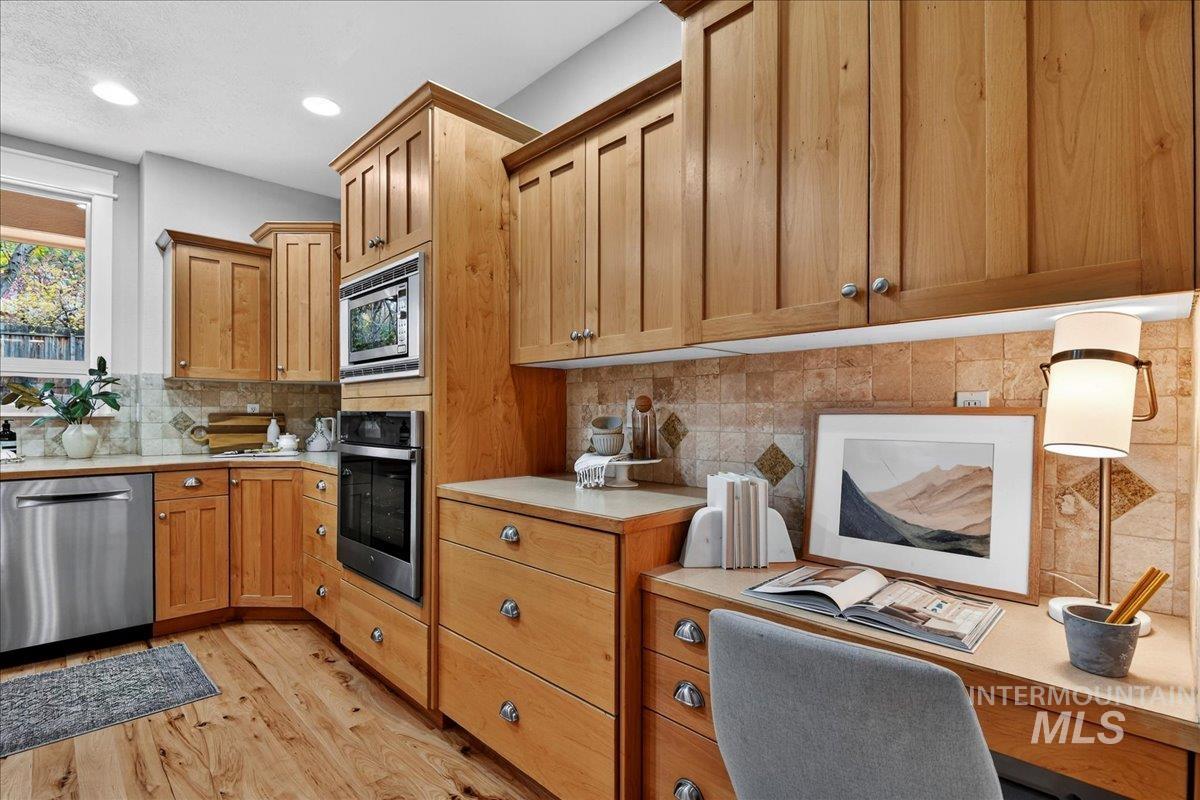 Kitchen with light countertops, stainless steel appliances, light wood-style floors, an office area, and brown cabinetry