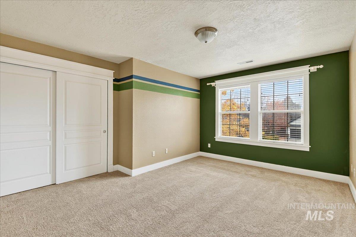 Unfurnished bedroom featuring a textured ceiling, light colored carpet, and a closet