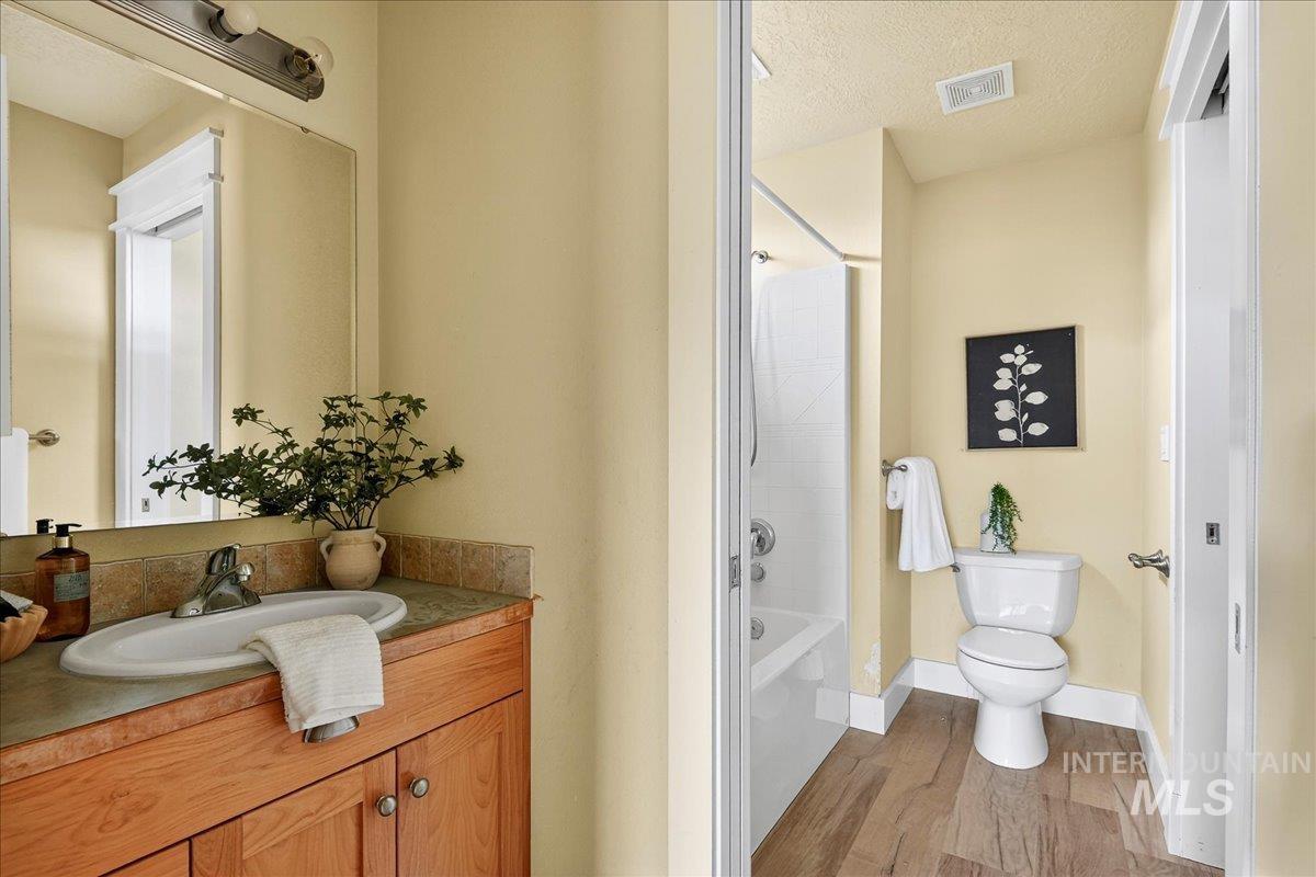 Bathroom with vanity, a textured ceiling, shower / tub combo, and light wood finished floors
