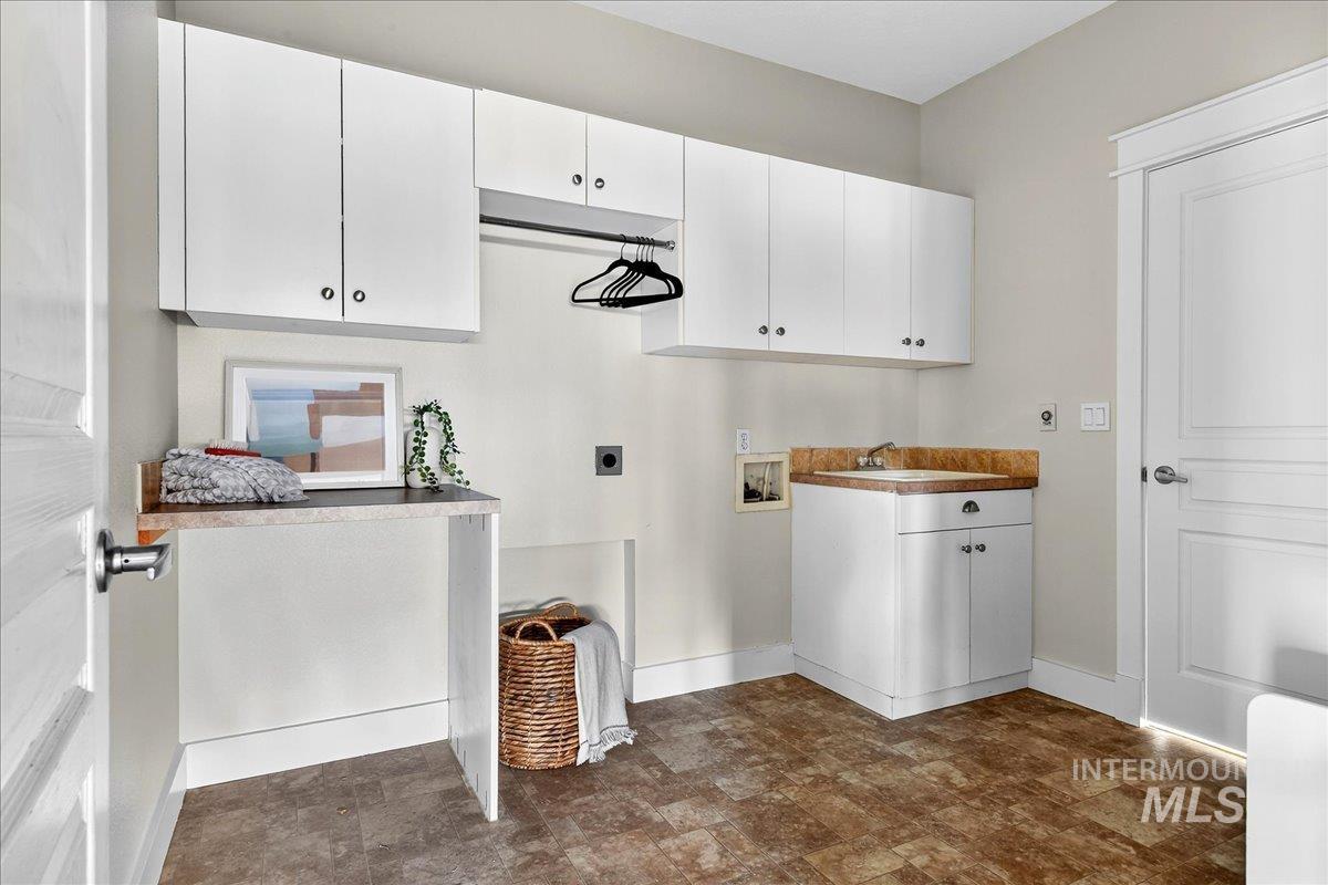 Washroom with hookup for a washing machine, electric dryer hookup, cabinet space, and stone finish flooring