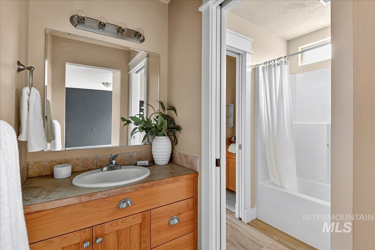 Bathroom with vanity, shower / bath combo with shower curtain, light wood-style flooring, and a textured ceiling