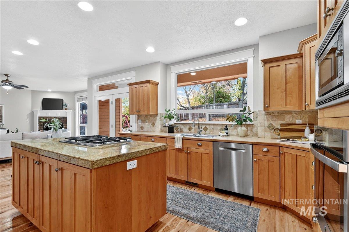 Kitchen featuring a fireplace, tile counters, light wood-style floors, stainless steel appliances, and recessed lighting