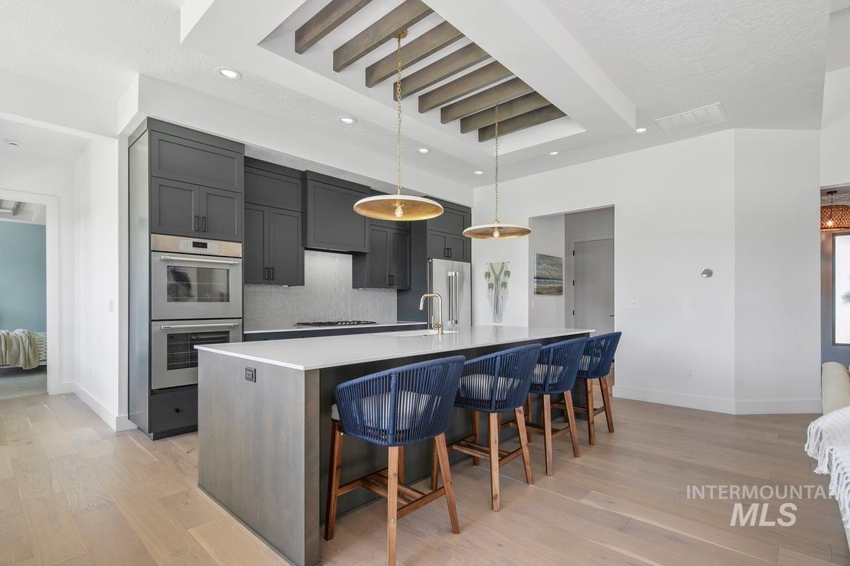 Kitchen with a kitchen breakfast bar, decorative backsplash, pendant lighting, a large island with sink, and stainless steel appliances
